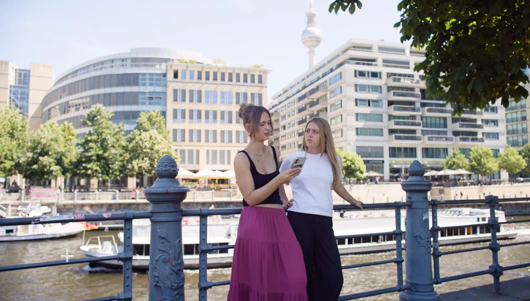 Two students in Berlin comparing notes on a phone by the river
